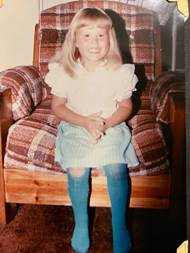 Lisa as a little girl, sitting in a plaid armchair