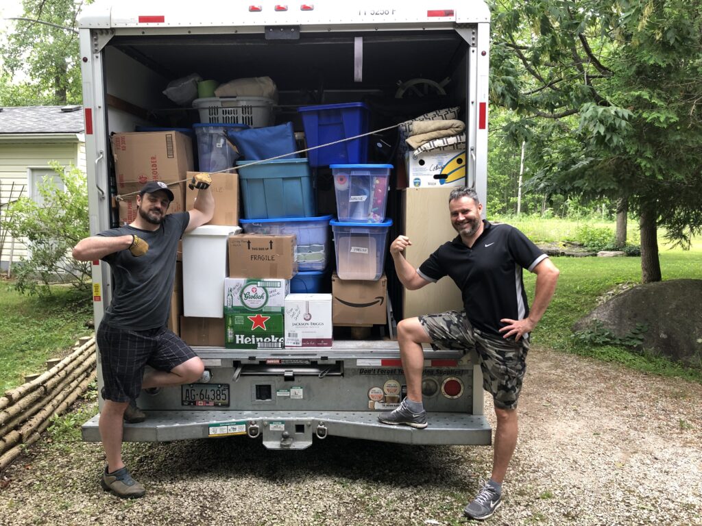 A moving truck packed full of boxes and bins, with two people posing proudly in front